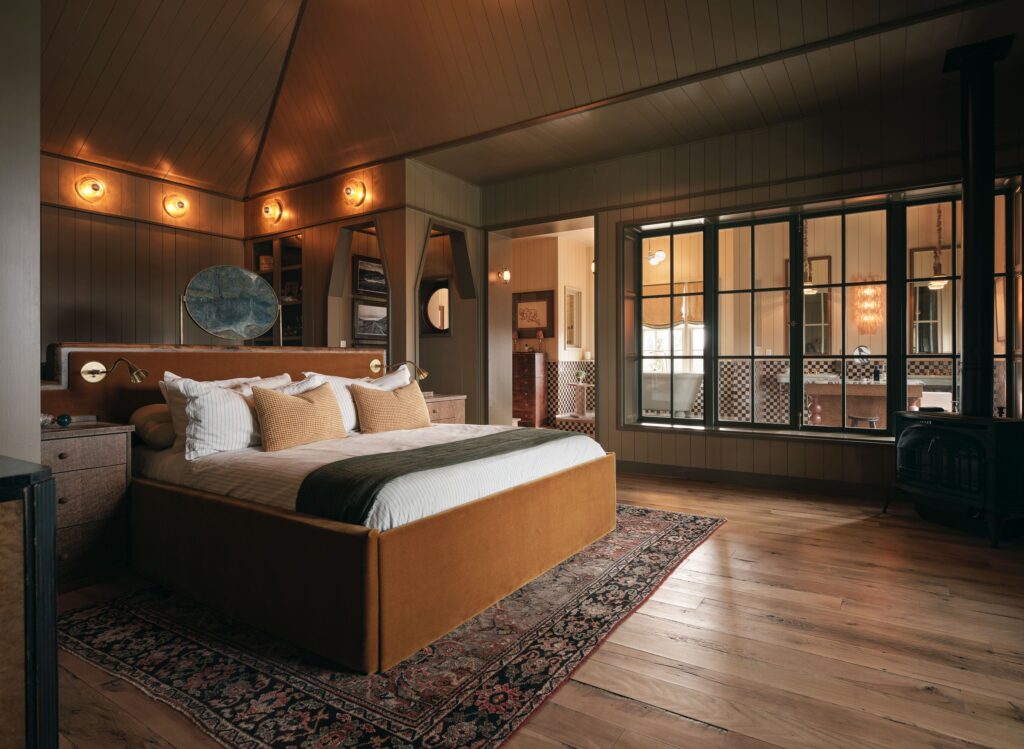 图案地毯上的木床架 白色床上用品 浴室配有棋盘瓷砖 透过窗户墙可以看到