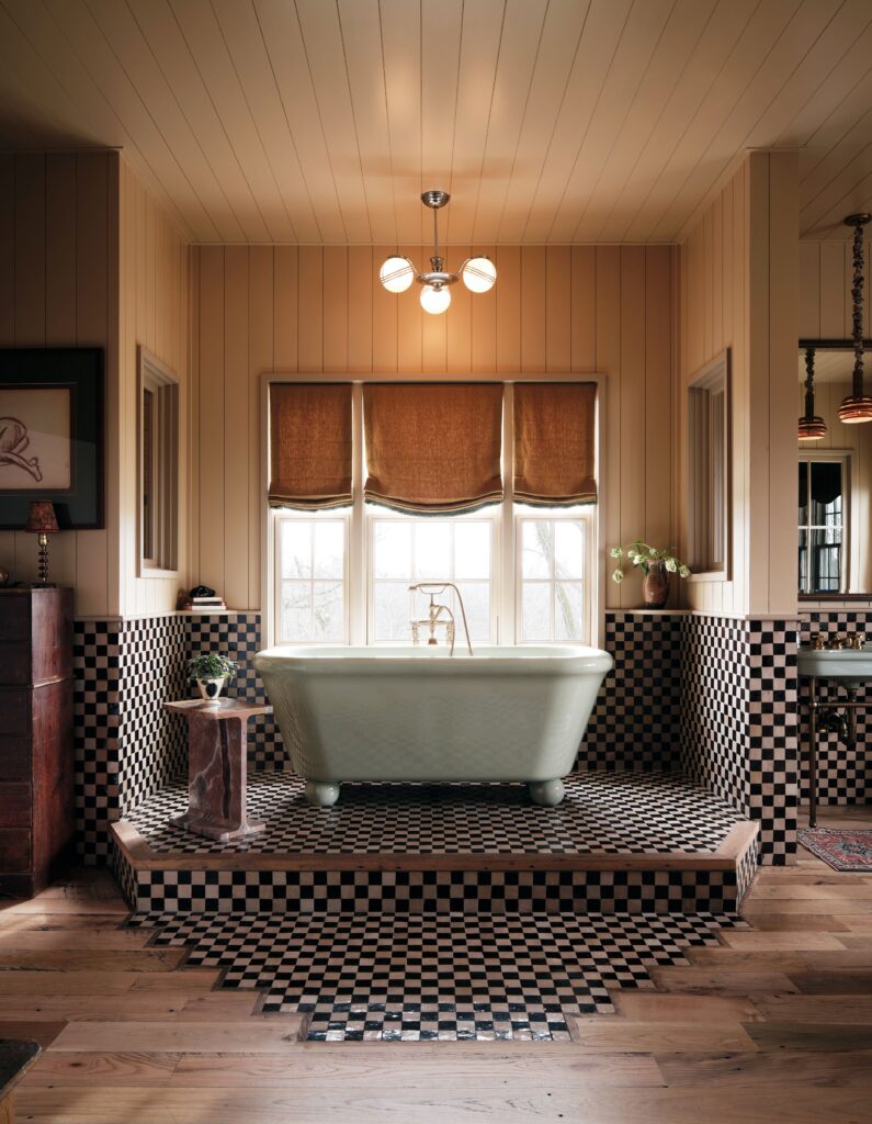 平台上的白色浸泡浴缸，带有棋盘格平铺窗户，棕色色调半拉小粉红色石头边桌......
